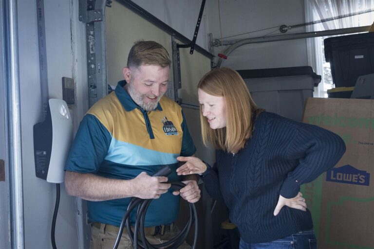A Thomas Edison Electric electrician showing a homeowner the connector on a Level 2 home EV charger.