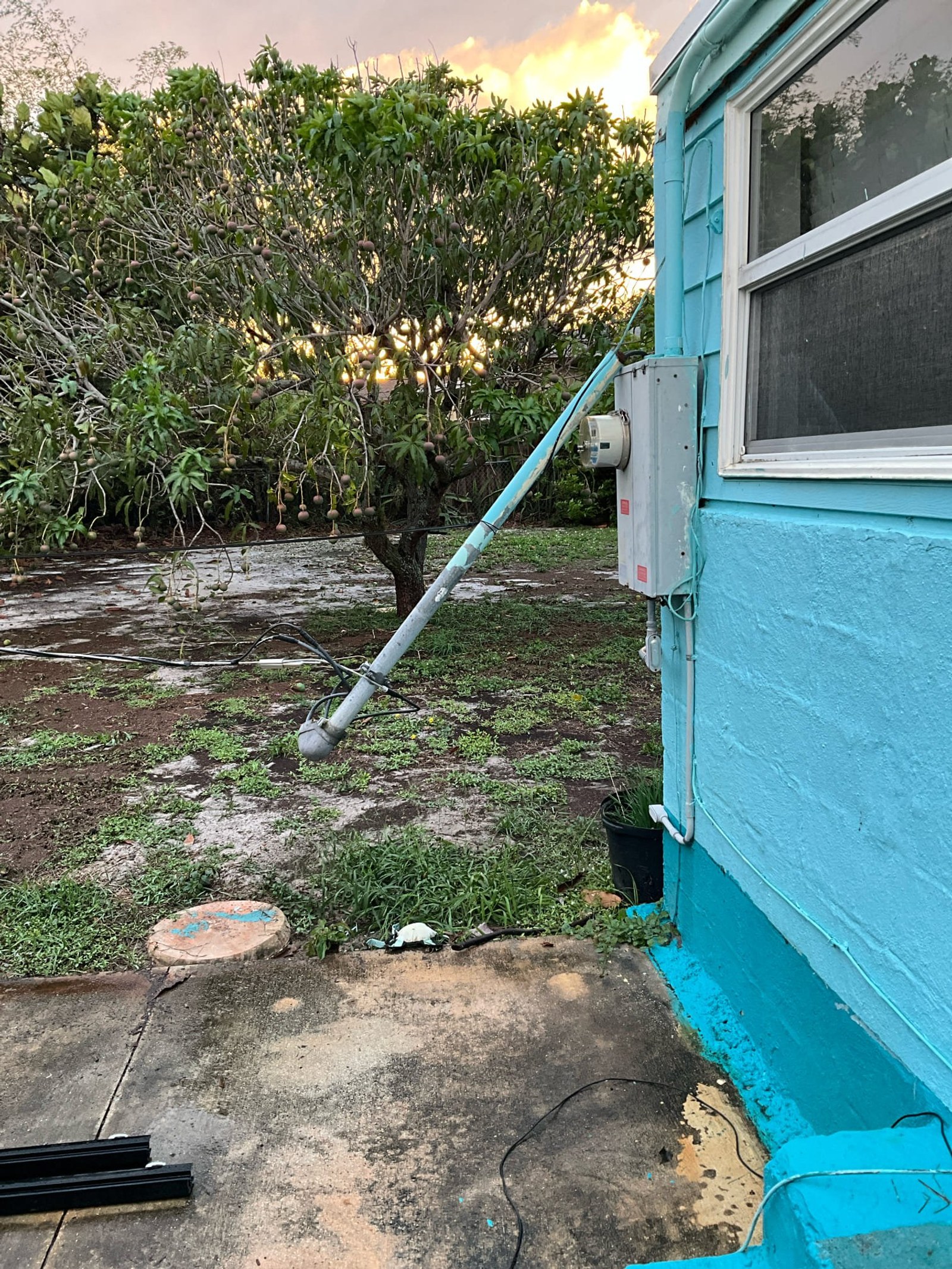Damaged meter base with broken conduit and exposed service line lying on ground outside building.