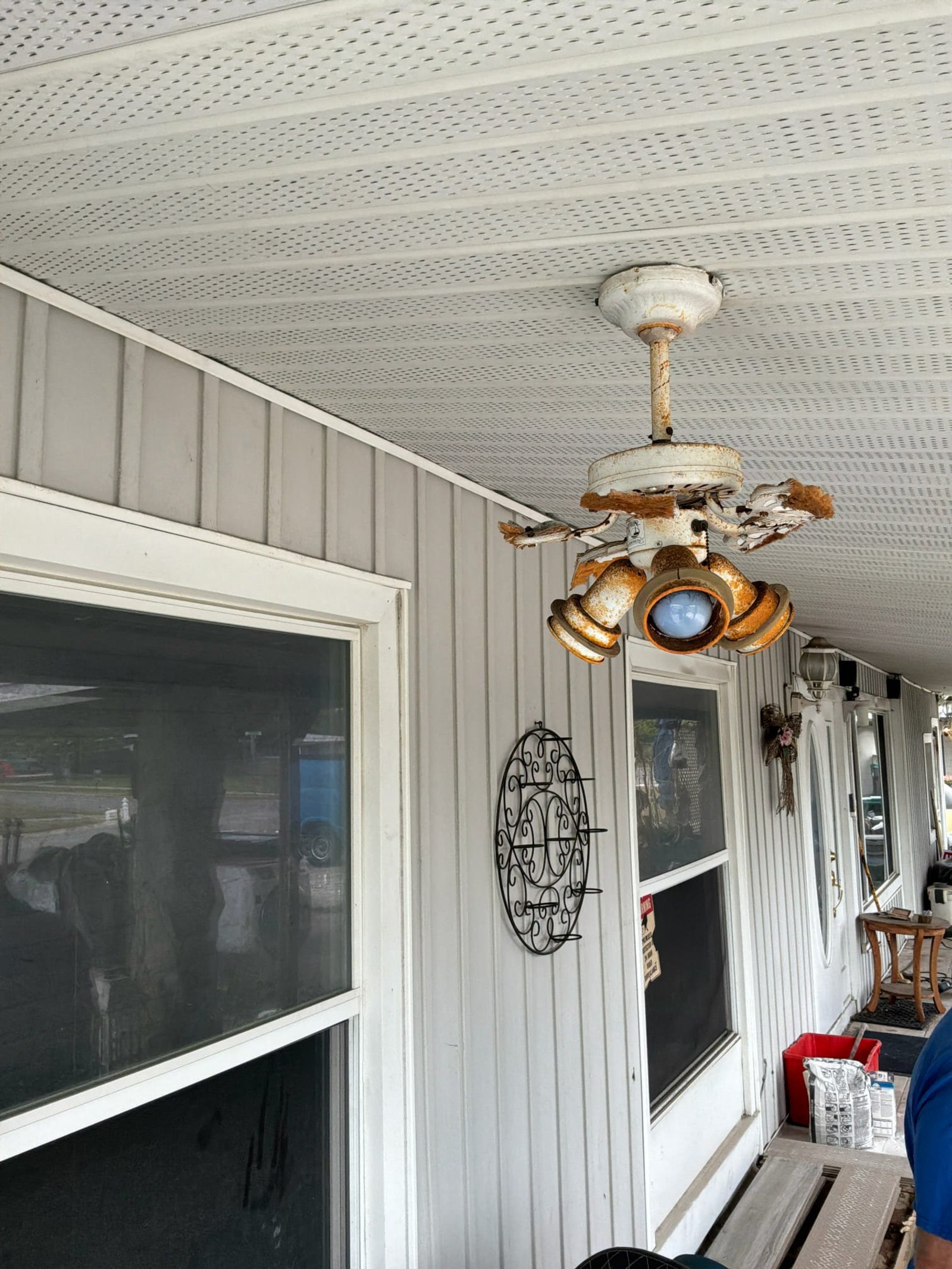 Corroded and deteriorated ceiling fan fixture with visible rust and peeling paint on mounting hardware.