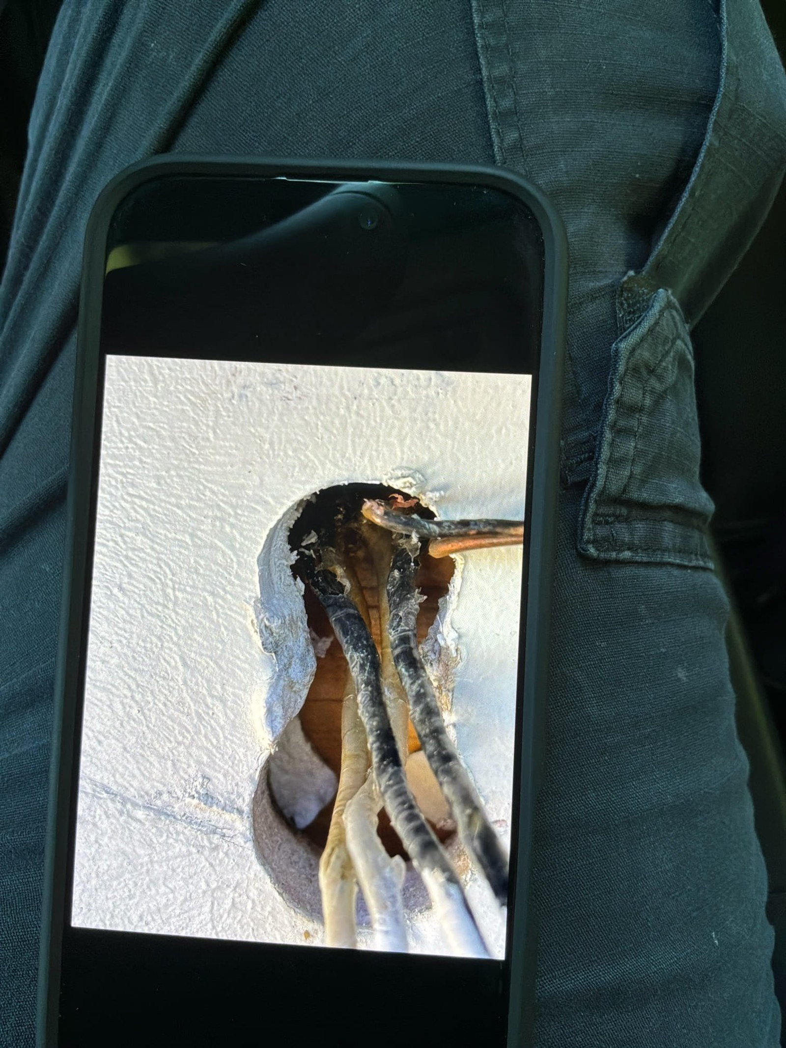 Phone close-up of corroded exterior fixture outlet with exposed copper wiring and blackened corrosion.