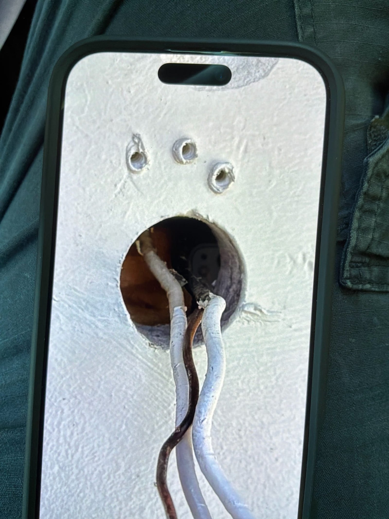 Phone close-up of exterior fixture junction box with three mounting holes and two corroded wires exiting opening.