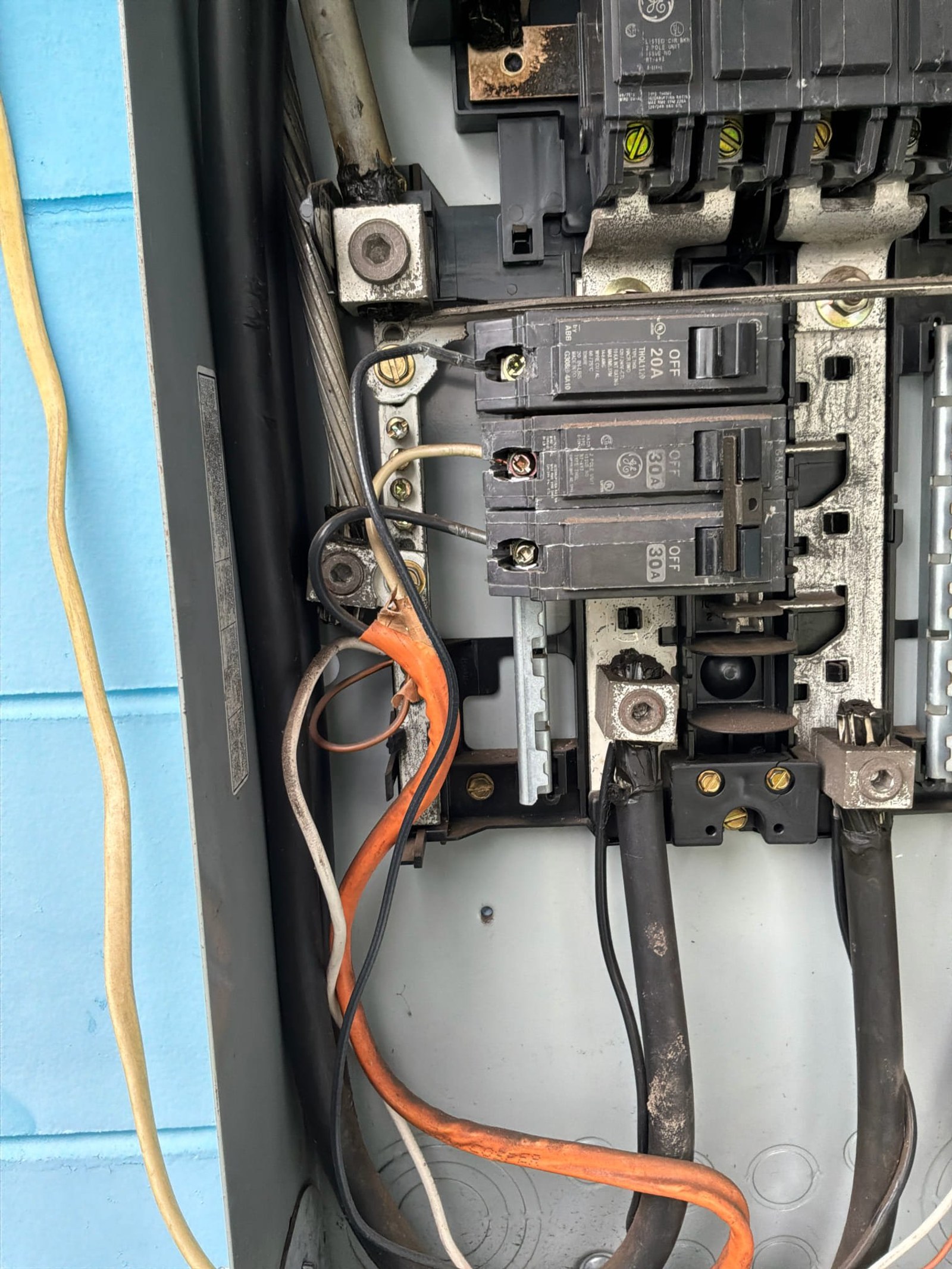 Panel interior showing multiple breakers with corrosion on lug connections and orange auxiliary wire.