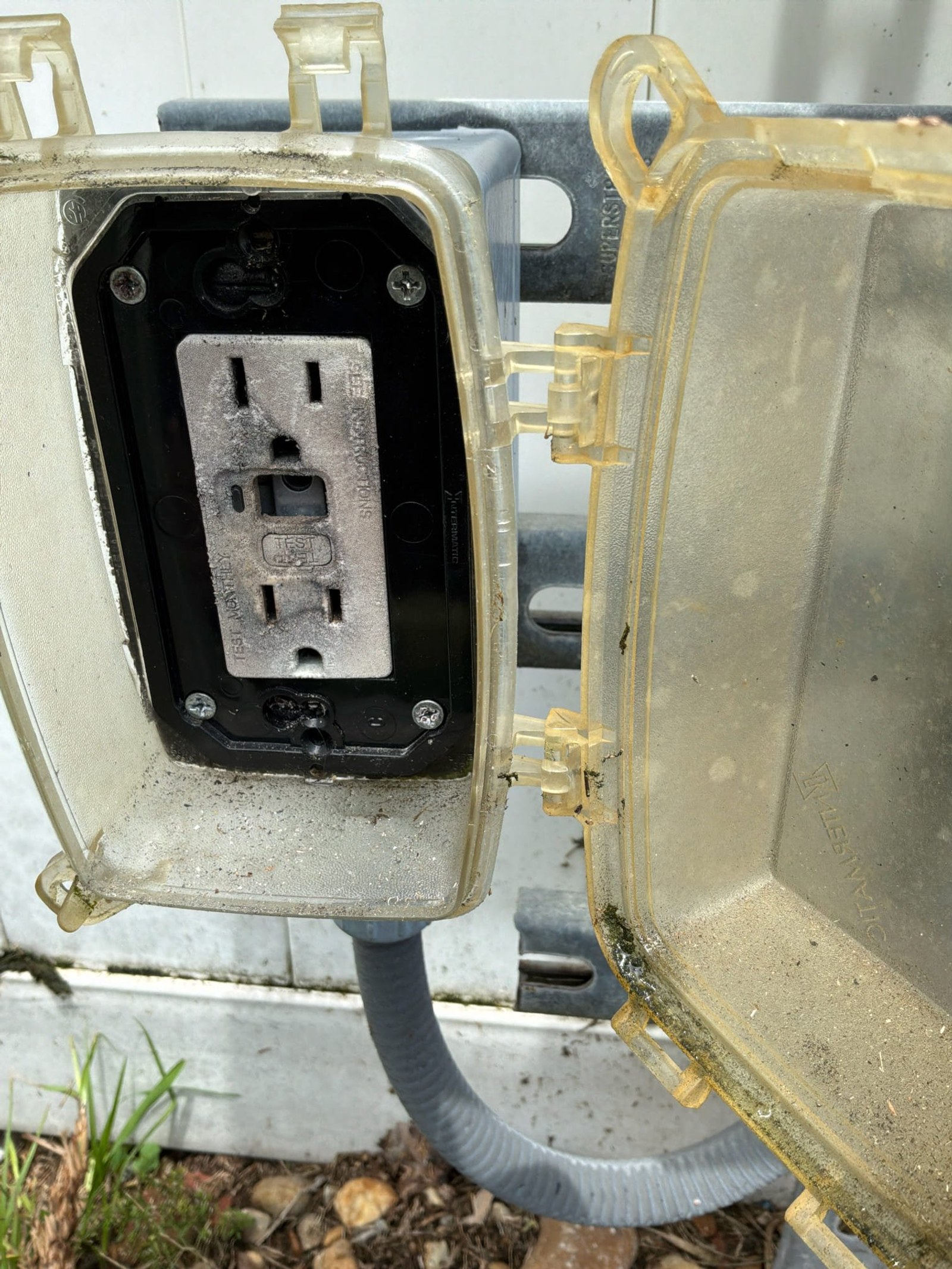 Exterior weatherproof outlet with rust-stained box showing non-GFCI protected receptacle and corroded mounting hardware.