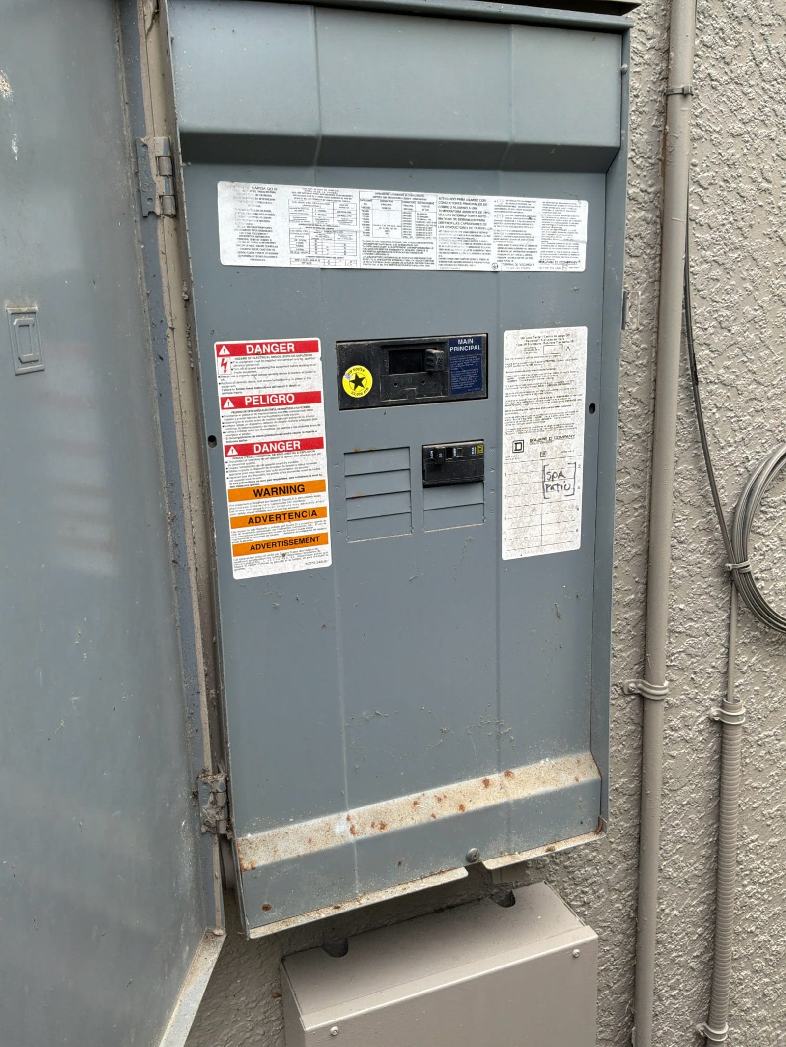 Exterior meter enclosure with main disconnect, bilingual warning labels, and specification documentation attached.