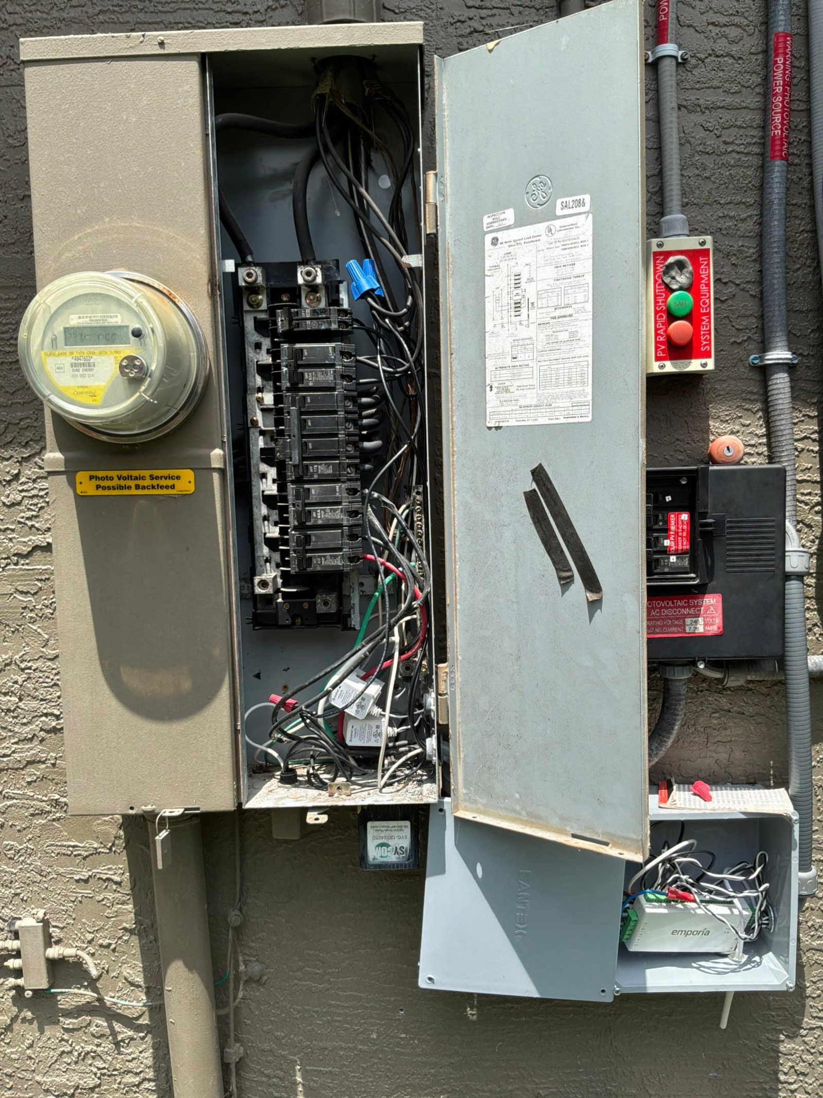 Main service panel interior with meter on left, multiple circuit breakers, and Emporia Vue 3 device installed below in dedicated enclosure with conduit connections.